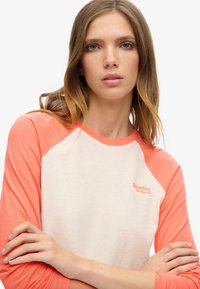 T-shirt met raglanmouwen in perzik- en creme-kleuren; zachte katoenen stof; met logo-detail op de borst; gevormde pasvorm.