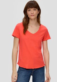Koraal gekleurd v-hals t-shirt met korte mouwen, voorzien van een zachte textuur en een afgeronde zoom. Gepaard met blauwe jeans.