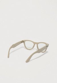 Beige plastik briller med katteøje-form, klare linser og en særlig metallisk logo detalje på stængerne, med en glat overflade.
