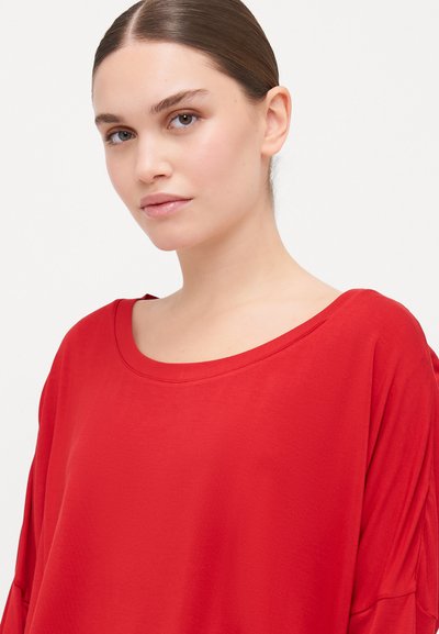Red, loose-fitting top with a wide neckline and short sleeves, made of soft fabric. Features a smooth texture and relaxed silhouette.