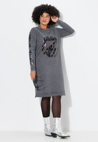 Robe grise en matière douce avec un design graphique rond et des accents brillants sur les manches. Assortie à des bottines argentées brillantes.