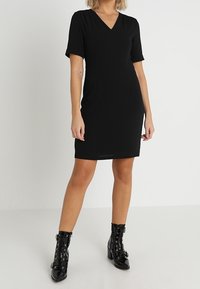 Svart kortärmad klänning med V-ringning och figurnära siluett. Kombinerad med blanka svarta snörstövlar till ankeln.