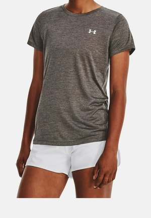 Personne portant un t-shirt de sport gris à manches courtes et un short blanc, debout avec les bras détendus le long du corps.