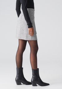 Falda de tweed gris con bolsillos, combinada con botas de cuero negras hasta el tobillo con tacón cuadrado. El modelo lleva una camiseta de manga larga negra y medias.