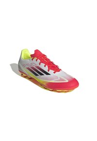 Jalkapallokenkä, jossa on valkoinen ja punainen päällinen, keltaiset yksityiskohdat ja mustat raidat. Rakenteellinen muotoilu, jossa on virtaviivainen muoto ja muotoillut piikit.