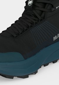 Κοντινό πλάνο ενός μαύρου και σκούρου τιρκουάζ παπουτσιού για πεζοπορία με χονδρές κορδόνια, ετικέτα Gore-Tex και υφασμένο πέλμα για εξωτερική χρήση.