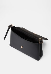 Čierna kožená kabelka s hladkou textúrou, so zlatým zapínaním a nastaviteľným popruhom. Interiér je podšitý čiernou látkou.