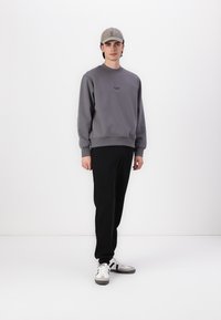 Grå sweatshirt med ribbede manchetter og kant, sorte bukser og grå kasket. Sneakers har hvidt skind med grå og sorte accenter.