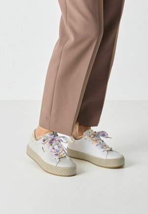 Hvide sneakers med snørebånd i blomstermønster, tekstureret beige platformsål og glat overdel. Kombineret med skræddersyede brune bukser.