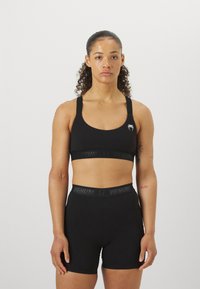 Conjunto de top desportivo preto e calções feitos de material elástico, com um logótipo no top e uma cinta com o nome da marca. Design simples.