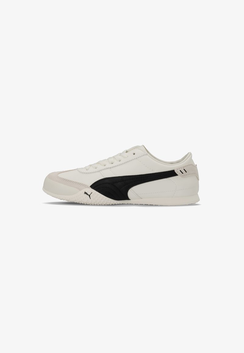 Baskets blanches à profil bas avec bande Puma noire sur le côté, lacets et semelle texturée, sur fond blanc uni.