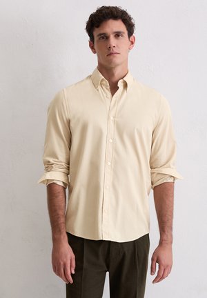 Lichtbeige overhemd met knopen en kraag, opgerolde mouwen en een gladde textuur, gecombineerd met donkergroene broek.
