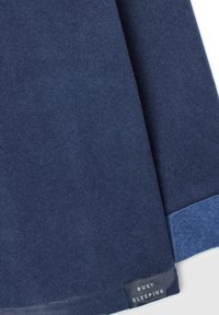 Navyblauwe katoenstof met een gestructureerde afwerking, met een contrasterende lichtblauwe zoom. Het etiket zegt "BUSY SLEEPING" in witte tekst.