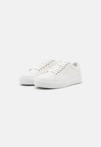 Sneaker bianche in tela con punta rotonda, suola piatta in gomma e chiusura con lacci. Presentano un logo discreto sul lato e un design minimalista.