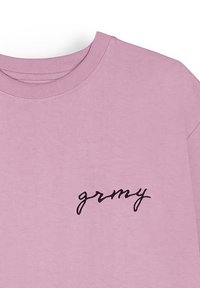 Camiseta de algodón rosa con cuello redondo y mangas cortas. Presenta el texto bordado en negro "grmy" en el área izquierda del pecho. Textura suave.
