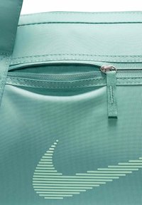 Fram zip-lomme av teal Nike-veske med sydd trekksnor og et foret swoosh-logo i teal på stoffoverflaten.