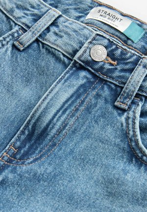 Közepes derekú egyenes farmernadrág elhalványult kék denimből, gombos záródással, narancssárga varrással és lapos derékkal, amelyen címke található.