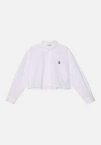 Chemise blanche courte à manches longues, col à boutons, boutons sur le devant, et un petit motif brodé sur la poitrine gauche.