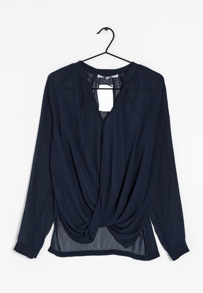 Blouse bleu marine à manches longues avec un design torsadé à l'avant suspendue sur un cintre noir sur fond blanc.