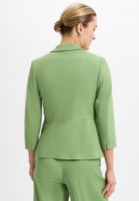 Hellgrüner Blazer mit taillierter Passform, Dreiviertelärmeln, subtiler Textur und Rückenschlitzdetail.