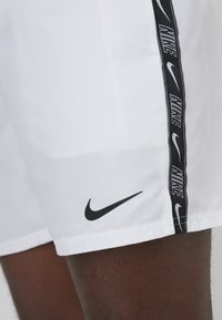 Pantalones cortos blancos de Nike con un logotipo negro y una franja lateral con el texto "Nike" en repetición. Tela suave, longitud por encima de la rodilla, corte entallado.