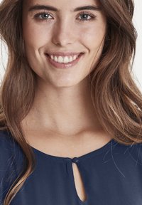 Blusa navy con scollatura a chiave e un piccolo dettaglio di bottone, realizzata in tessuto leggero, con texture liscia e un morbido drappeggio.