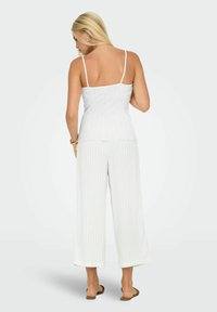 Biała, prążkowana kamizelka na cienkich ramiączkach, w połączeniu z szerokimi spodniami w delikatne pionowe paski. Gładka tekstura; casualowy design.