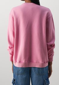 Pink crewneck sweatshirt with long sleeves and ribbed cuffs. Features a brushed texture with a relaxed fit. Back view shows smooth fabric.