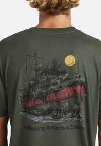 Oliivroheline T-särk, millel on vintage laeva graafika, täiendatud taimede ja punase vööndiga, mida toob esile kollane päike ja must tekst.
