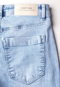 Jasnoniebieskie dżinsy o klasycznym kroju, z tylną kieszenią i metką na pasku z napisem "STREET ONE". Gładka tekstura.