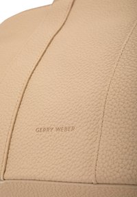 Superficie in pelle beige testurizzata con il marchio "GERRY WEBER" in rilievo e dettagli di cucitura visibili.