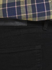 Black jeans with a textured finish, featuring a back pocket and a leather label. A plaid shirt in navy, yellow, and pink is layered above.