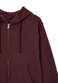 Felpa con zip color marrone bordeaux, dotata di cappuccio regolabile con coulisse, tasche frontali e tessuto morbido e testurizzato. Presenta una zip argentata e un design semplice.