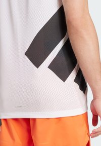 White mesh sports top with black diagonal stripes, featuring a textured surface. Paired with bright orange shorts, showing a casual athletic look.