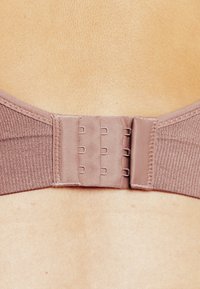 Primo piano di un gancetto di un reggiseno beige abbottonato su pelle nuda, con tre file di ganci e occhi sul retro.