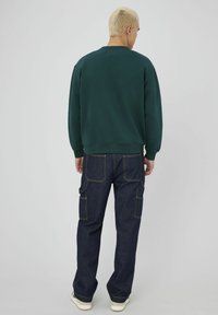Un sweat-shirt vert avec des poignets et un ourlet côtelés, associé à un pantalon cargo en denim bleu foncé avec de multiples poches et des accents de couture clairs.