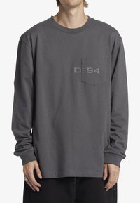 Grå långärmad t-shirt med rund halsringning, framficka och subtil "Dc94" grafik på bröstet. Tillverkas av bomull, avslappnad passform.