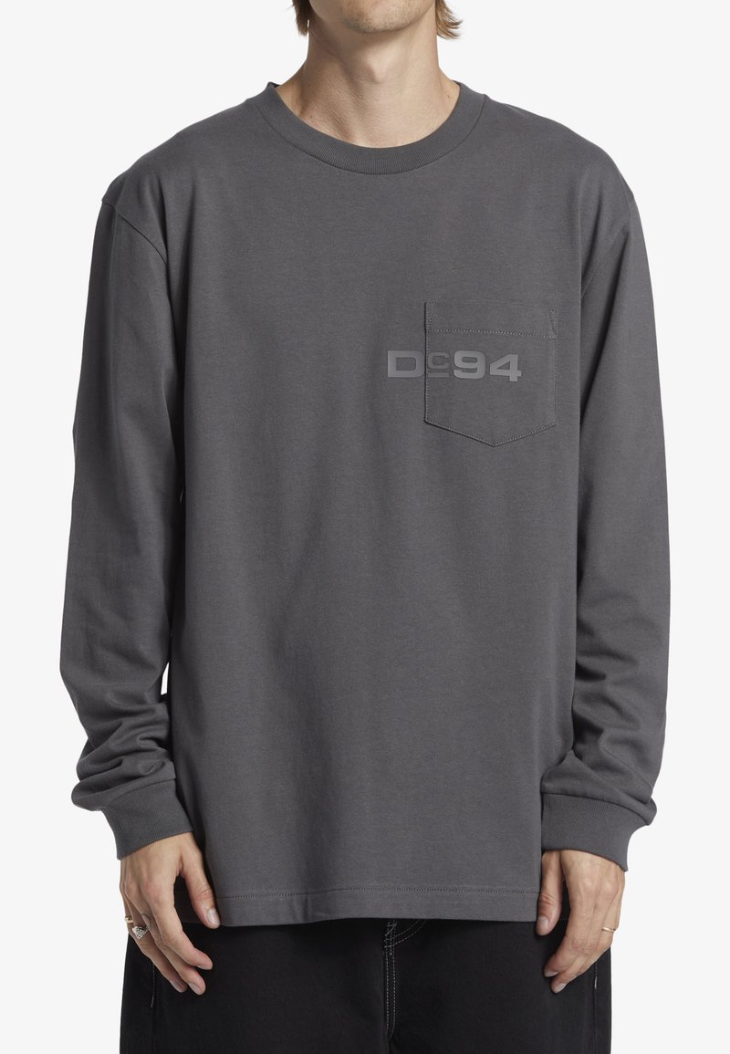 Grå långärmad t-shirt med rund halsringning, framficka och subtil "Dc94" grafik på bröstet. Tillverkas av bomull, avslappnad passform.