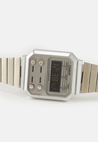 Montre numérique Casio avec un boîtier octagonal argenté, un bracelet en acier inoxydable, un affichage noir et deux boutons à l'avant pour les fonctions et les réglages.