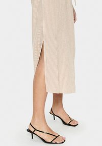 Randig midi-klänning i ljusbeige och krämfärgad med sidesslits; matchad med svarta sandaler med hög klack och remmar; slät tygstruktur.