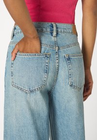 Svetlomodré denimové džínsy so zvýšeným pásom, širokými nohavicami a dvoma zadnými vreckami s viditeľným prešitím.