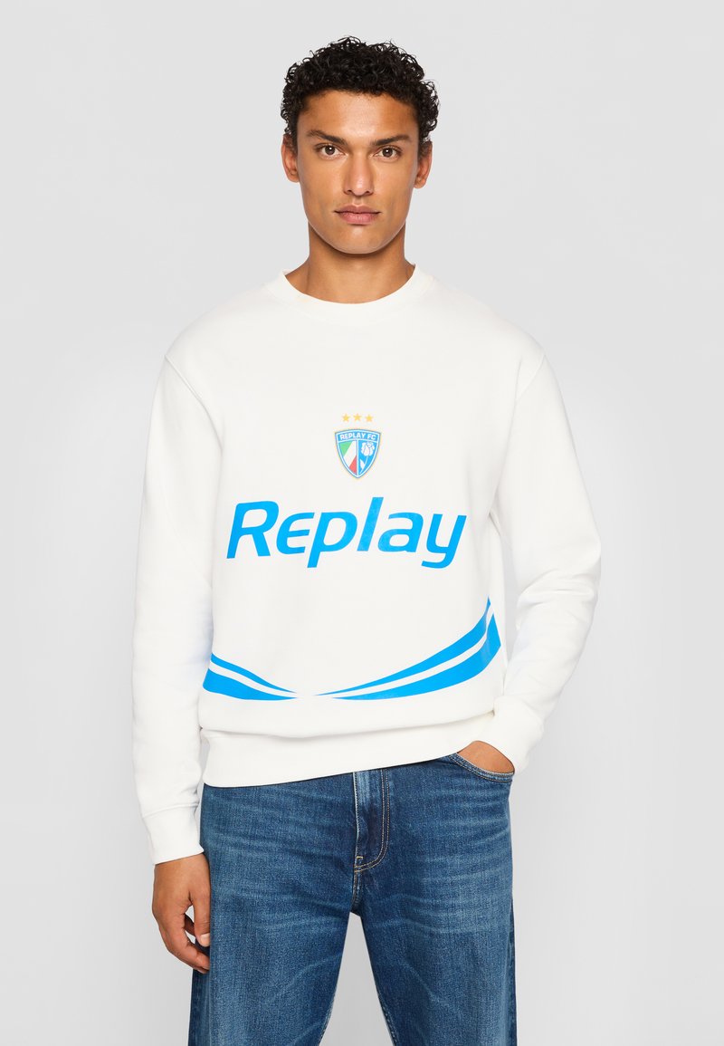 Hvid sweatshirt med blåt "Replay" logo og buede detaljer, med rund halsudskæring og ribbede manchetter, kombineret med blå jeans.