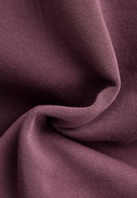 Tejido suave y texturizado en un color mauve profundo, con un patrón de punto suave, con suaves pliegues y curvas que destacan su caída.