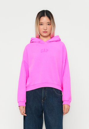 Rosa hætte sweatshirt med "GAP" logoet i en matchende nuance, designet med cropped længde og afslappet pasform. Pariert med mørke denim bukser.
