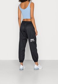 Svarta träningsbyxor med elastiska muddar och midja, med en vit logotyp. Bärs tillsammans med en ljusblå ribbad croppad topp och vita sneakers.