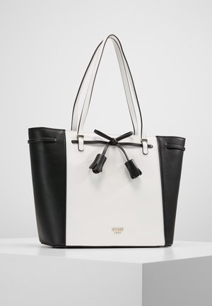 Torba typu tote w czarno-białym kolorze z dwoma uchwytami, dekoracyjną czarną kokardą w kształcie kwiatów oraz małym złotym logo na środku z przodu.