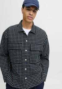 Camicia nera con bottone, decorata con un motivo a griglia bianca, presenta due tasche sul petto e un colletto. Tessuto morbido con una vestibilità comoda.