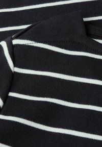 Zwarte stof met horizontale witte strepen. Zachte textuur, met een ronde halslijn en nette stiksels langs de randen.