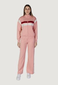 Completo sportivo rosa chiaro con giacca con zip caratterizzata da strisce rosse e bianche, abbinato a pantaloni coordinati. Realizzato in tessuto morbido con vestibilità comoda.