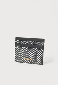 Μαύρος και άσπρος υφασμάτινος θήκης καρτών με δύο υποδοχές για κάρτες και χρυσό λογότυπο "Coccinelle" σε ανοιχτό φόντο.